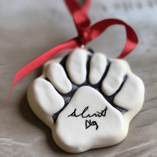 A finished DIY dog paw print ornament made from salt dough, painted and decorated with the dog's name and a ribbon.